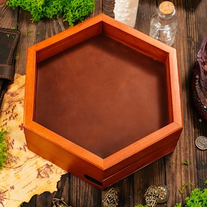 May include: A hexagonal wooden dice tray featuring a smooth, dark brown leather interior base and a polished light brown wooden frame. The tray is designed with six straight sides and is empty, showcasing the contrast between the wood and leather.