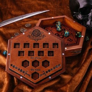 Könnte beinhalten: Eine Holzkiste mit einem Scharnierdeckel, die einen Satz Würfel enthält. Die Kiste hat ein Fach für Trefferpunkte und Trefferwürfel. Der Deckel trägt den Text "YOU CAN CERTAINLY TRY".