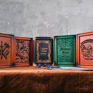 May include: A collection of five wooden boxes with framed artwork and text. The boxes are in various colors, including brown, orange, green, and black. The artwork includes a crossed hammer and sword design, a monster illustration, and the text "Alchemy Book".