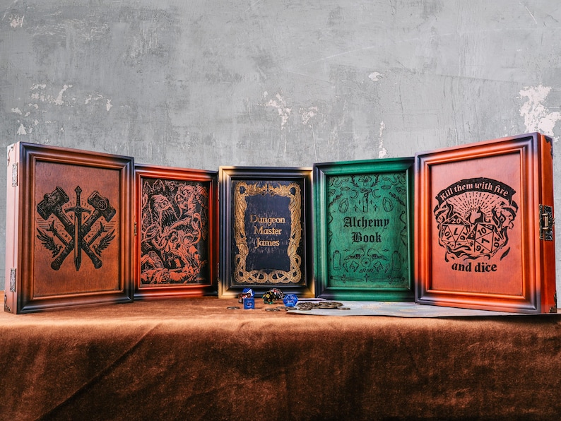 May include: A collection of five wooden boxes with framed artwork and text. The boxes are in various colors, including brown, orange, green, and black. The artwork includes a crossed hammer and sword design, a monster illustration, and the text "Alchemy Book".