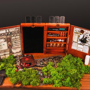 May include: A wooden tabletop gaming organizer with a central tablet slot, shelves for small glass vials, and two hinged side panels displaying character sheets. The unit features clear acrylic dividers at the top and is surrounded by green moss.