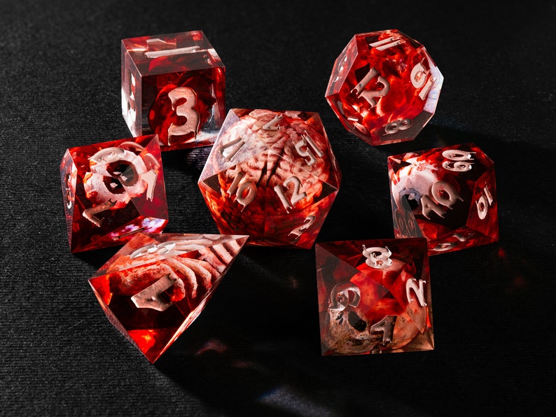 Puede incluir: Un juego de siete dados poli&eacute;dricos hechos de resina roja transl&uacute;cida. Cada dado contiene un modelo en miniatura de un cerebro humano suspendido en su interior. Los n&uacute;meros est&aacute;n grabados con un acabado plateado met&aacute;lico en las caras.