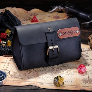 May include: A matte black leather pouch with a front buckle closure and a brown leather patch featuring the text SHOT and a geometric icon. The pouch is constructed with visible stitching along the edges and secured with metallic rivets and a buckle.