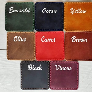 May include: A set of eight square leather coasters with rounded corners and visible stitching. The colors are labeled as Emerald, Ocean, Yellow, Olive, Carrot, Brown, Black, and Vinous. Each coaster features a smooth, matte finish and a distinct color.