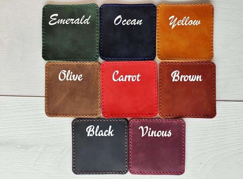 May include: A set of eight square leather coasters with rounded corners and visible stitching. The colors are labeled as Emerald, Ocean, Yellow, Olive, Carrot, Brown, Black, and Vinous. Each coaster features a smooth, matte finish and a distinct color.