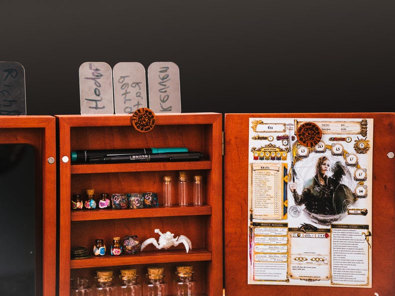 May include: A wooden tabletop gaming organizer with three shelves containing small glass vials, multi-sided dice, and a white creature figurine. The right panel features a character sheet with an illustration of a warrior, and the top has name tags.