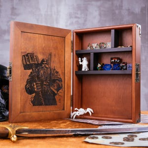 May include: A wooden dice box with a hinged door featuring an engraved image of a bearded warrior holding a hammer. The open box reveals shelves with dice and figurines. The box is brown with a dark interior.