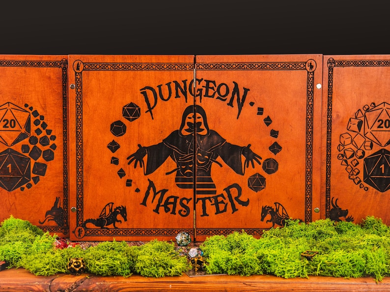 May include: A folding wooden dungeon master screen with a dark brown finish. The center panel features a black laser-engraved graphic of a hooded figure, the text "DUNGEON MASTER," and various polyhedral dice. Side panels show large d20 dice.