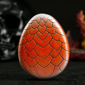 May include: A red and silver dragon egg with a textured, scaly surface. The egg is a decorative object.