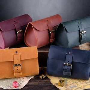 May include: Five rectangular leather pouches with rounded sides, each featuring a single flap secured by a metal buckle strap. The pouches are colored in shades of deep purple, reddish-brown, dark green, mustard yellow, and navy blue.