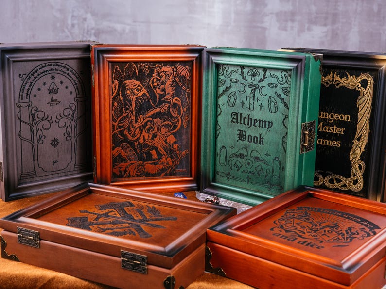 May include: Wooden game boxes with engraved designs. The boxes are various colors, including brown, green, and black. Some boxes have text that reads "Alchemy Book" and "Dungeon Master Games". The boxes are designed for board games.