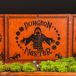 May include: Wooden Dungeon Master screen with a dark orange finish. The screen features a black graphic of a robed figure and the words "Dungeon Master". Dice and dragon illustrations are also present. The screen is decorated with green moss.
