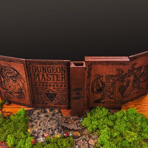 Peut inclure: Un &eacute;cran de ma&icirc;tre de donjon en bois marron avec des illustrations fantastiques grav&eacute;es et le texte "DUNGEON MASTER". L'&eacute;cran est ouvert, r&eacute;v&eacute;lant un bac &agrave; d&eacute;s et une carte de jeu miniature. De la mousse verte et des pi&egrave;ces de jeu sont au premier plan.