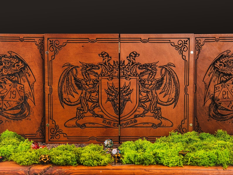 May include: A four-panel wooden dungeon master screen featuring laser-engraved dragon illustrations and a central crest with the text DM THOMAS. The panels are connected by metal hinges and display intricate border patterns on a medium brown wood finish.