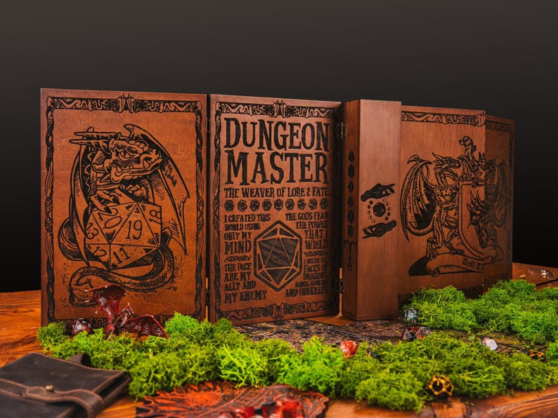 Peut inclure: &Eacute;cran de ma&icirc;tre de donjon en bois marron, avec des illustrations grav&eacute;es de dragons et de d&eacute;s. Le panneau central affiche le texte "DUNGEON MASTER". L'&eacute;cran est pos&eacute; sur une table en bois, orn&eacute;e de mousse verte.