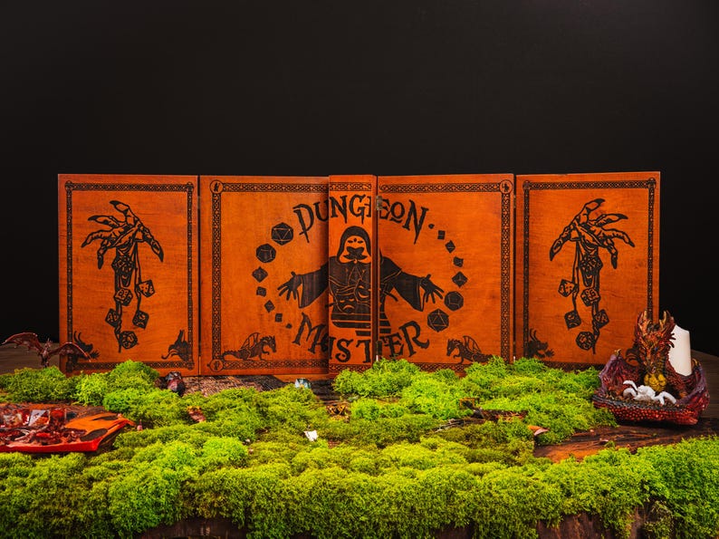 Peut inclure: Un &eacute;cran de ma&icirc;tre de donjon orange avec des illustrations et du texte noirs. L'&eacute;cran est entour&eacute; de mousse verte, avec un bougeoir dragon et d'autres accessoires sur le th&egrave;me de la fantaisie.