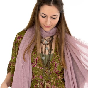 May include: A woman wearing a layered necklace with coin pendants, a green paisley print dress, and a light purple scarf. The necklace has multiple strands of varying lengths. The dress has a V-neck and long sleeves.
