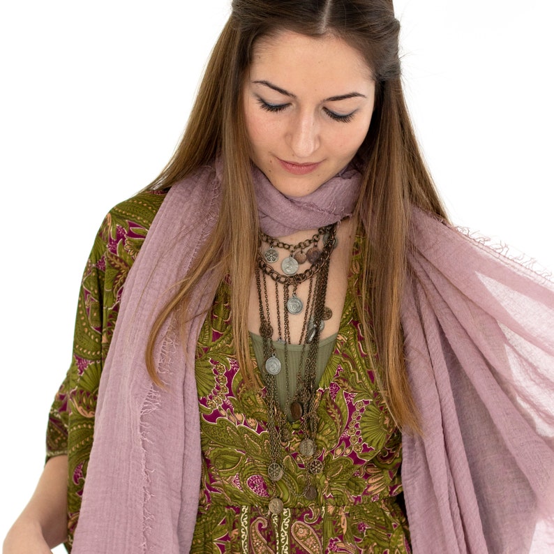 May include: A woman wearing a layered necklace with coin pendants, a green paisley print dress, and a light purple scarf. The necklace has multiple strands of varying lengths. The dress has a V-neck and long sleeves.