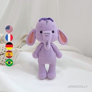 Könnte beinhalten: Ein gehäkeltes lila Elefantenspielzeug mit rosa Ohren und einem lila Haarknoten. Der Elefant hat schwarze Augen und einen gestickten Mund.