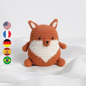 May include: A crocheted fox plush toy with a white chest and orange fur. The toy is sitting on a white surface.