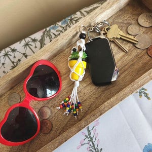 May include: A white macrame keychain with a small yellow and green potted plant charm. The keychain has colorful beads and is attached to a silver key ring with keys.