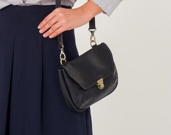 Puede incluir: Una blusa gris claro con cuello mandarín y bordados florales. La blusa tiene manga larga y cierre de botones. La modelo lleva un bolso bandolera negro.