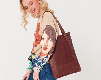 May include: A woman wearing a beige sweater with a colorful print and blue jeans is carrying a brown leather tote bag.
