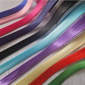 May include: An assortment of satin ribbons in a spectrum of colours, such as pink, blue, purple, and green. The ribbons are displayed diagonally, highlighting their smooth texture and vivid hues. Suitable for crafting and decorative purposes.