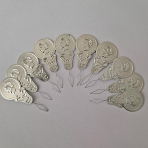 May include: A set of 12 silver needle threaders with a decorative design. Each threader has a small loop at the end of the needle for easy threading.