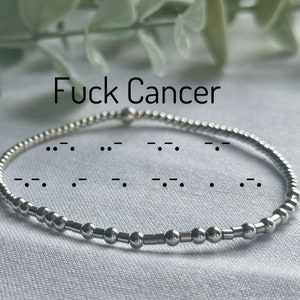 May include: A silver bracelet with a message in braille that reads "Fuck Cancer".