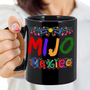 May include: Black ceramic mug with the word "MIJO" in red, purple, and green, and the word "Mexico" in colorful letters. The mug is decorated with floral designs.