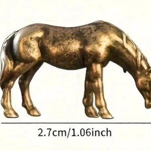 Puede incluir: Figura de camello de color bronce, de 2,7 cm de largo, 1,7 cm de alto y 0,7 cm de ancho. El camello est&aacute; representado en una pose de pastoreo, con la cabeza baja. La figura tiene una textura detallada y probablemente es de metal.