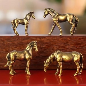 Puede incluir: Cuatro peque&ntilde;as figuras de caballos de color bronce en varias poses. Dos caballos est&aacute;n de pie, uno est&aacute; pastando y el &uacute;ltimo est&aacute; en posici&oacute;n de caminar. Las figuras son detalladas y parecen ser de metal.