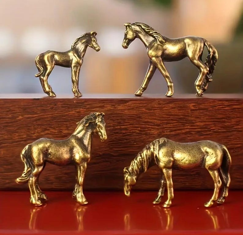 Puede incluir: Cuatro peque&ntilde;as figuras de caballos de color bronce en varias poses. Dos caballos est&aacute;n de pie, uno est&aacute; pastando y el &uacute;ltimo est&aacute; en posici&oacute;n de caminar. Las figuras son detalladas y parecen ser de metal.