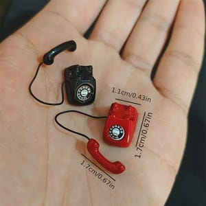 Puede incluir: Miniaturas de tel&eacute;fonos de estilo vintage en negro y rojo. El tel&eacute;fono rojo mide 1,7 cm de alto y el tel&eacute;fono negro mide 1,1 cm de alto. Cada tel&eacute;fono tiene un auricular y un dial. Los tel&eacute;fonos son peque&ntilde;os y detallados.