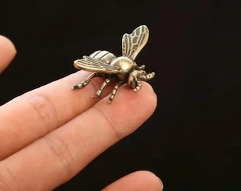 May include: A small, detailed brass bee figurine with intricate wing and body details. The bee is posed as if in flight, with its wings slightly spread. The figurine is a warm, metallic gold color.