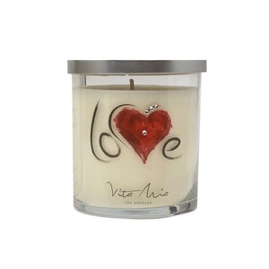 May include: A glass candle jar with a silver lid. The candle is white and has a red heart with the word "love" written in black script around it. The jar has the words "Vita Mia Los Angeles" printed on the bottom.