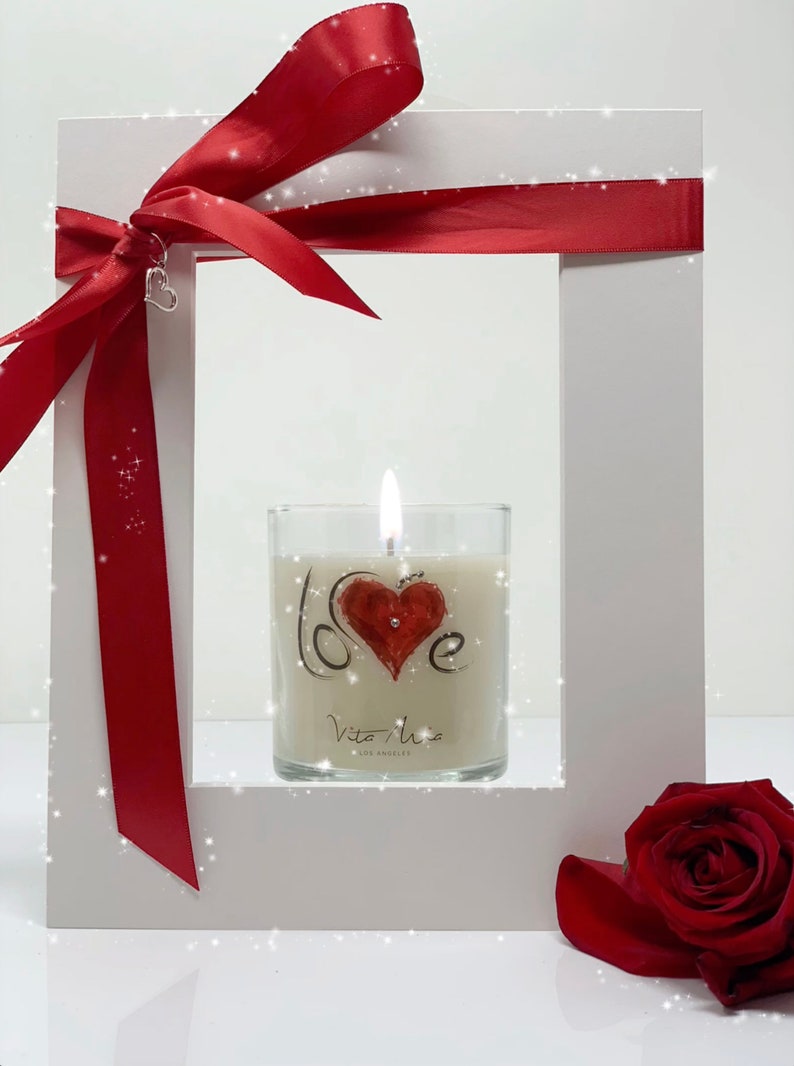 White frame with a red ribbon. In the center of the frame is the Vita Mia love candle adorned with Swarovski crystals.