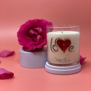 "Love candle:" A translucent label adorned with Swarovski crystals. Beneath is a white lid. To the left, a white pedestal and a gorgeous flower.