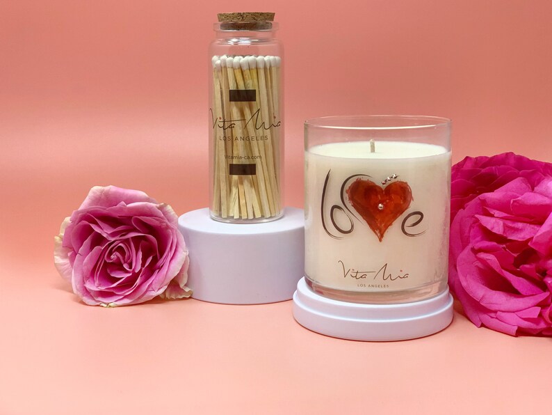 Candle gift set: a black sleek gift set adorned with a red ribbon. Love candle adorned with a clear label. Beneath, a black and white box. A white tip 4in matchstick in a glass vial