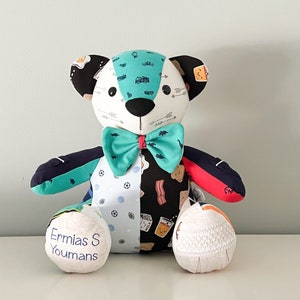 May include: A handmade patchwork teddy bear with a teal bow tie. The bear's head features a mix of patterns, including arrows, trucks, and eggs. The bear's body is split with different patterns, and the feet have embroidered text.