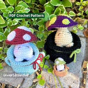 Könnte beinhalten: Drei gehäkelte Pilz-Amigurumi-Spielzeuge. Der größte Pilz ist lila und grün mit einem weißen Gesicht und sitzt in einem schwarzen gehäkelten Topf. Der mittlere Pilz ist rot und weiß mit einem blauen Gesicht und sitzt in einem blauen gehäkelten Topf. Der kleinste Pilz ist grün und weiß und sitzt in einem braunen gehäkelten Topf. Das Bild enthält den Text "PDF Crochet Pattern" und "@cmartdesignshop".