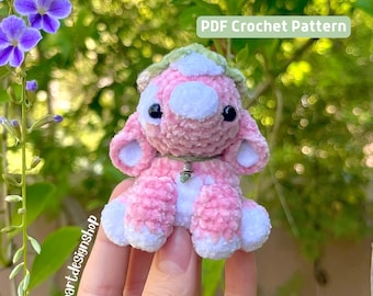 May include: A pink and white crocheted amigurumi cow with a green leaf headband. The cow is sitting on a hand and has black eyes. The text "PDF Crochet Pattern" is in the upper right corner of the image.