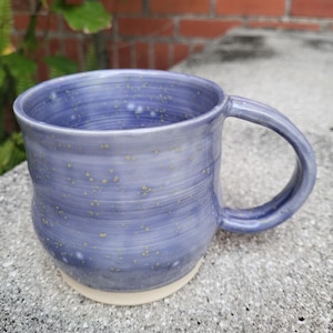 May include: A blue ceramic mug with a speckled glaze and a white rim. The mug has a rounded body and a handle.