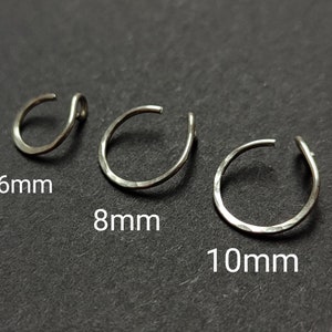 Op de afbeelding: Drie zilveren neusringen, 6 mm, 8 mm en 10 mm in diameter, op een donkergrijs oppervlak.