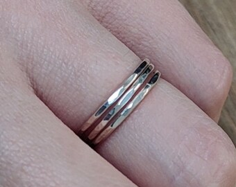 Puede incluir: Tres anillos apilables de plata martillados en un dedo.