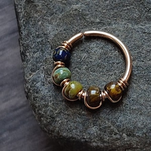 May include: Gold hoop earring with a row of colorful glass beads. The beads are green, blue, and brown.