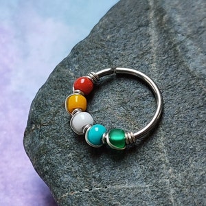 May include: A silver nose ring with a rainbow of coloured beads. The beads are yellow, orange, white, turquoise, and green.
