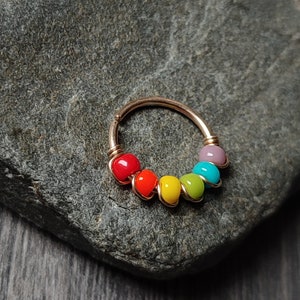Könnte beinhalten: Ein goldener Nasenring mit einem Regenbogen aus bunten Perlen. Die Perlen sind rot, orange, gelb, grün, blau und lila.