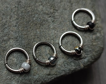 May include: Five silver hoop earrings with different colored beads. The beads are black, white, gray, and a multi-colored swirl.